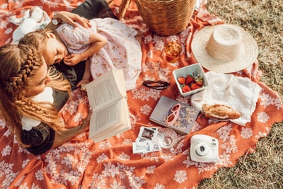 躺在橘色和白色的花卉野餐垫上和女孩一起读书的女人